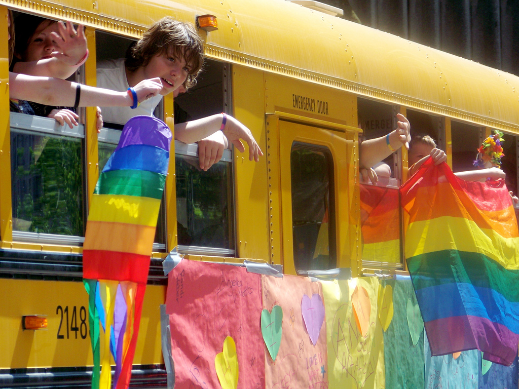 Children hanging rainbow flags out of a bus window