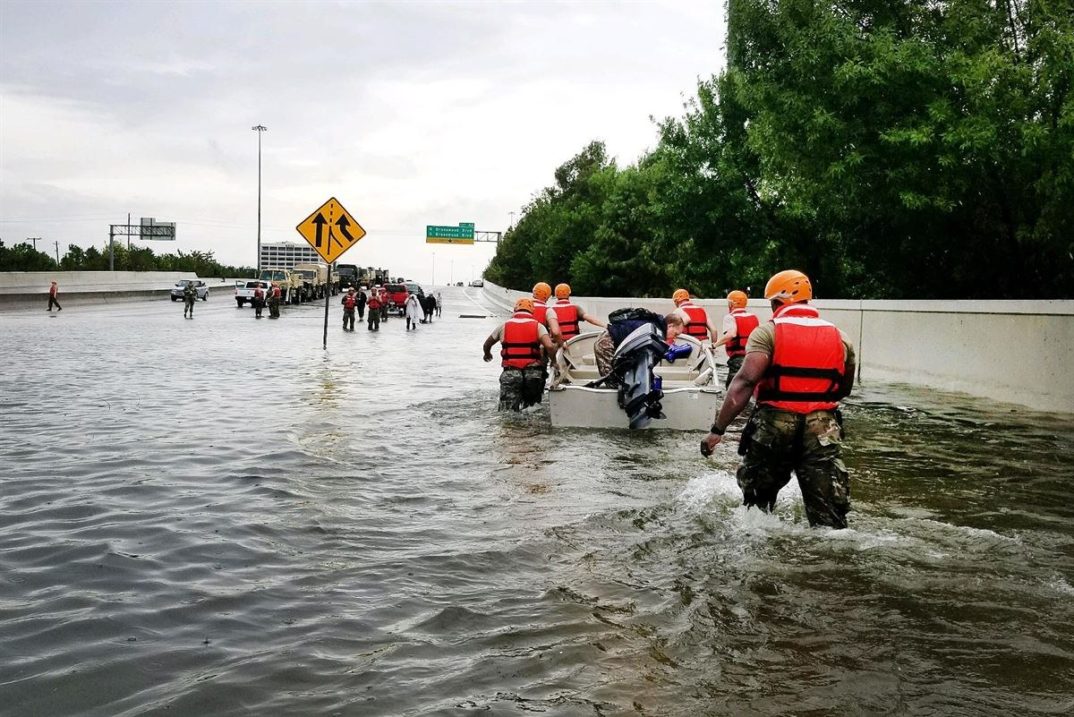 A photo of National Guard members helping people on a flooded highway overpass.