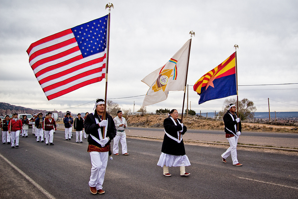 A photo of Native Americans marching along a highway with flags.