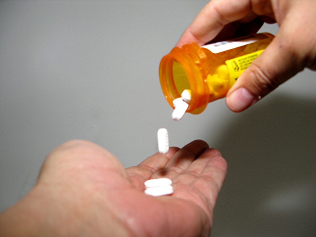 An image of a person pouring pills from a prescription bottle into their hand.