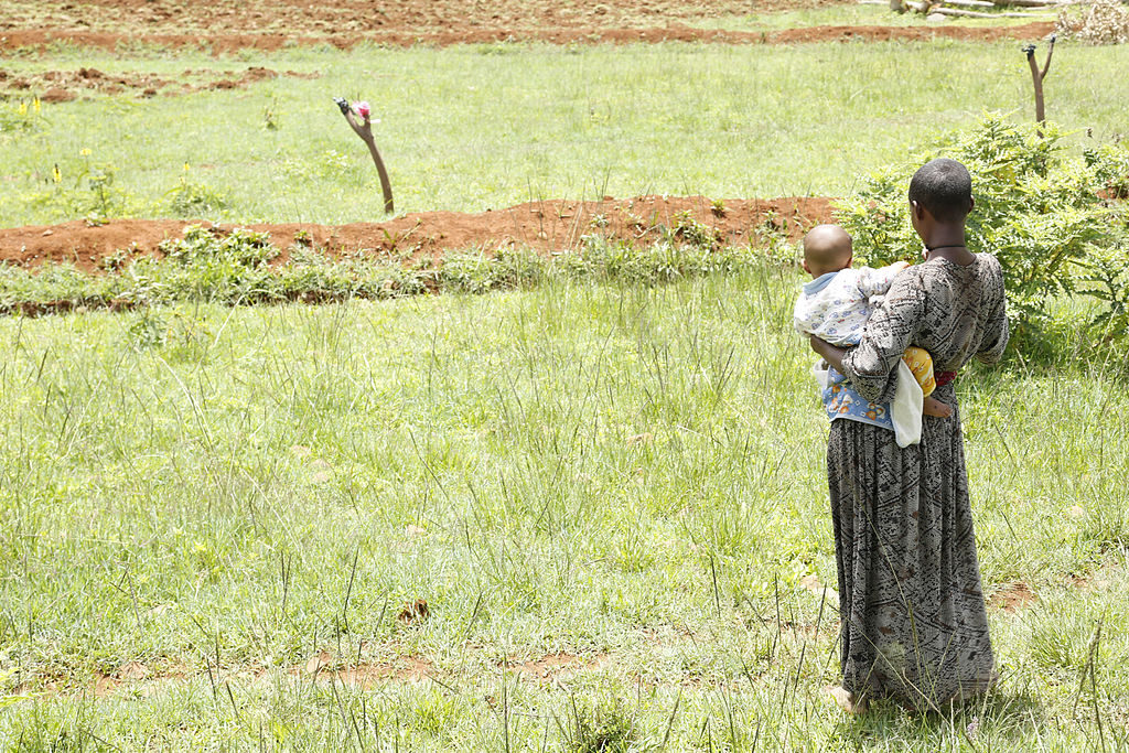 A photo of an African woman looking out over a field with her baby.
