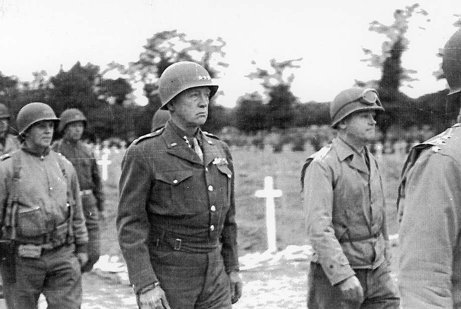 A black-and-white photo of George Patton marching through a cemetery.