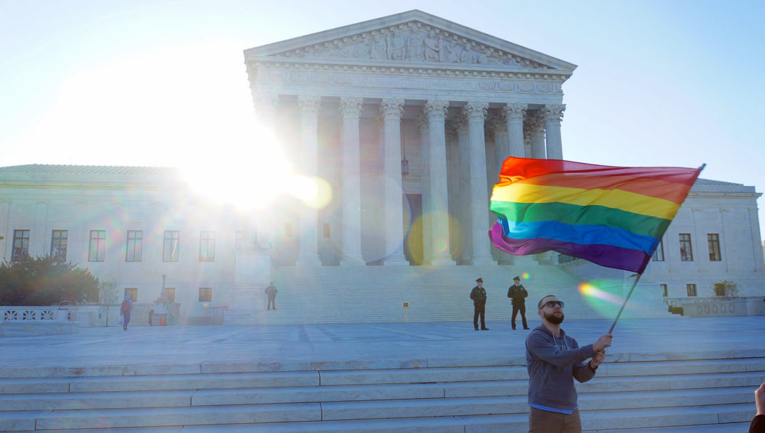 A photo of a man waving an LGBTQ+ rainbow flag outside the Supreme Court
