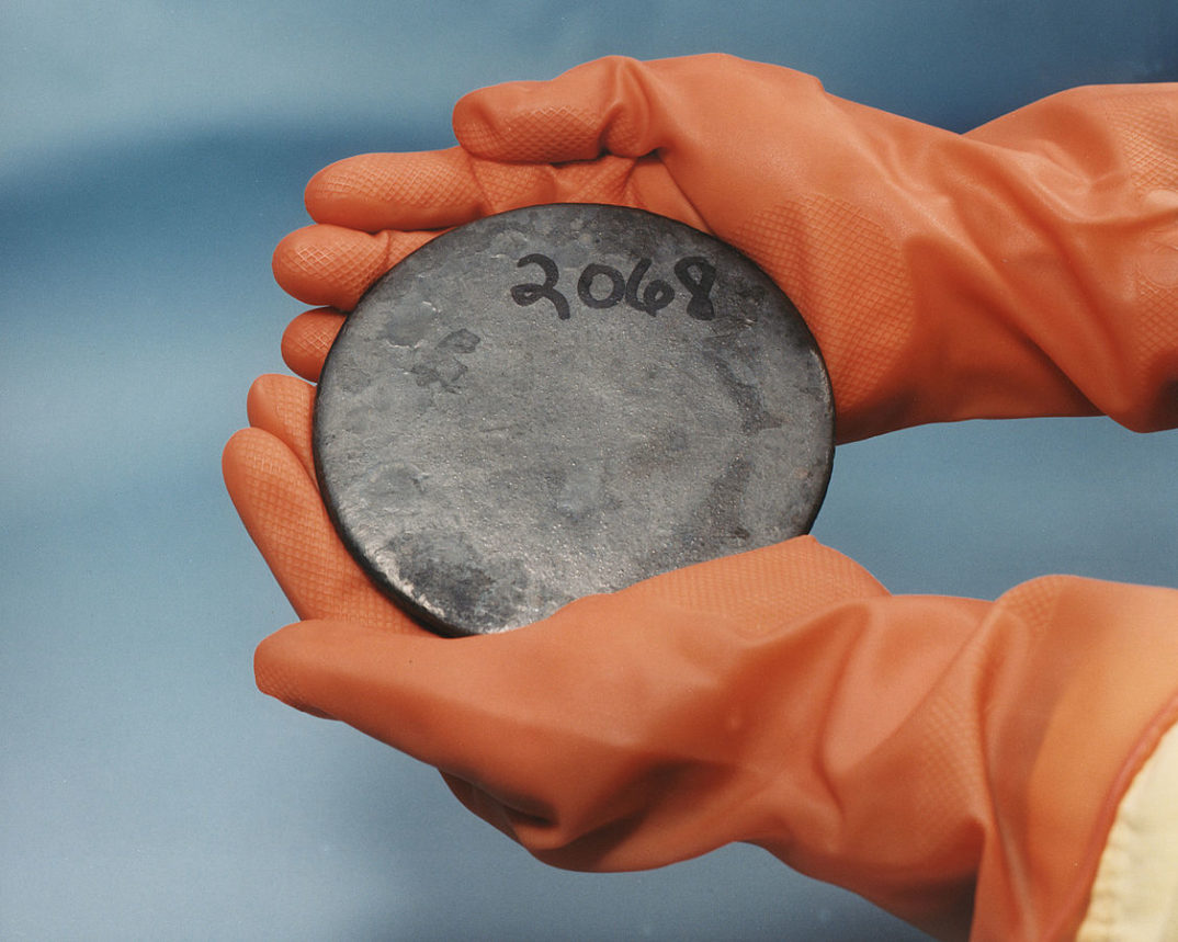 Two gloved hands holding a circular plate of uranium.