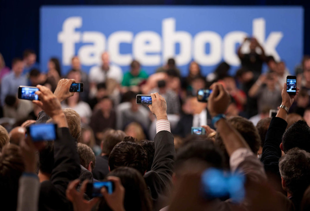 A photo of reporters taking pictures of the Facebook logo with their phones.