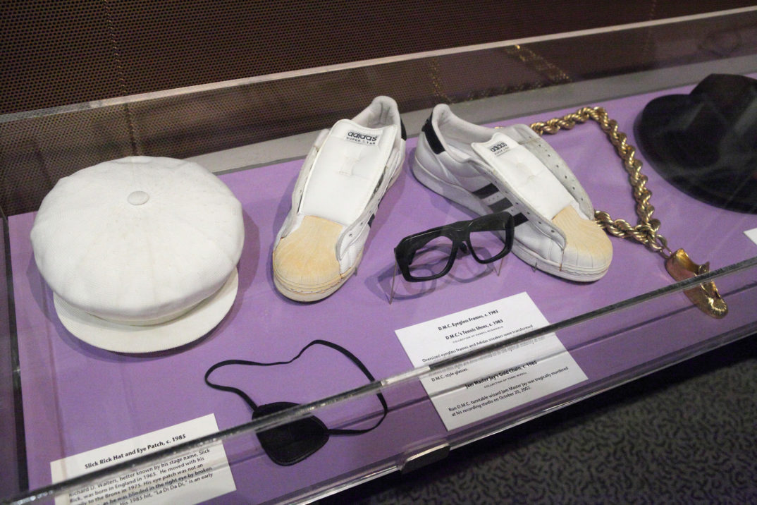 Image of a hat, eye patch, tennis shoes, gold necklace, and top hat displayed in glass case