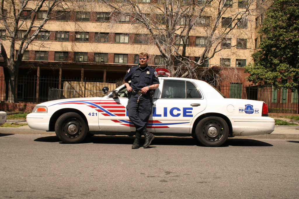 Photograph of a police officer leaning against a police car