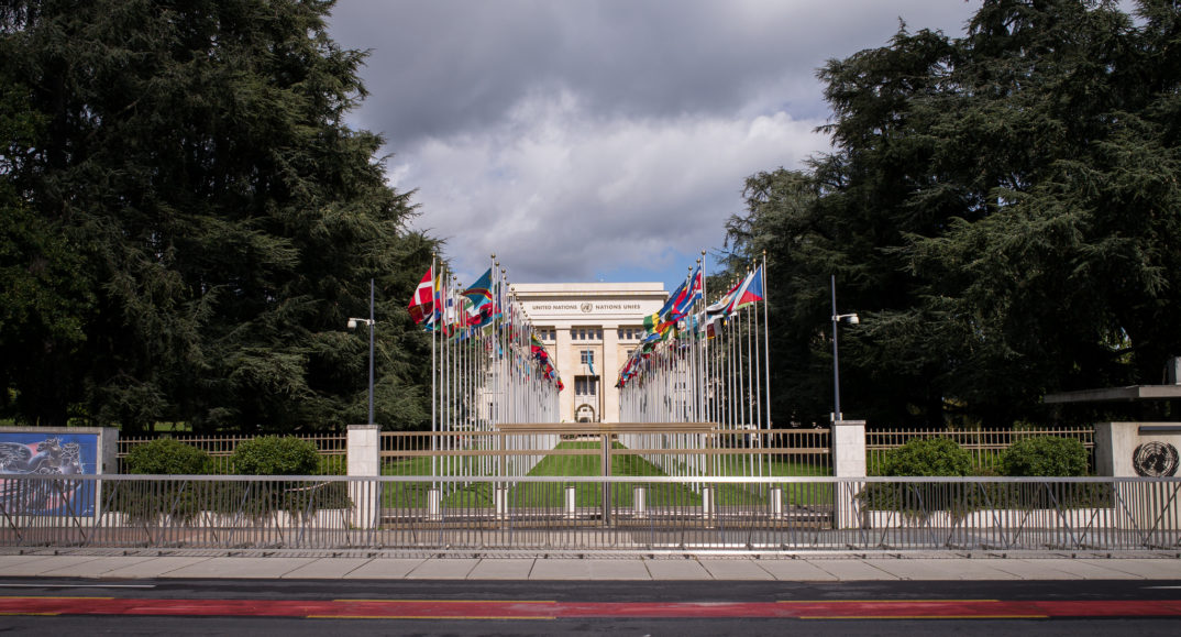Photograph of Palais des Nations building with flags in two columns in front of it