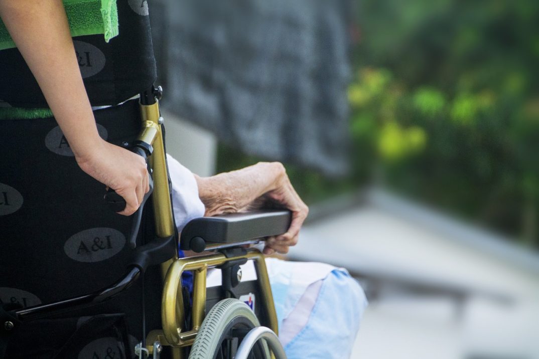 Image of a caretaker wheeling an elderly person in a wheelchair.