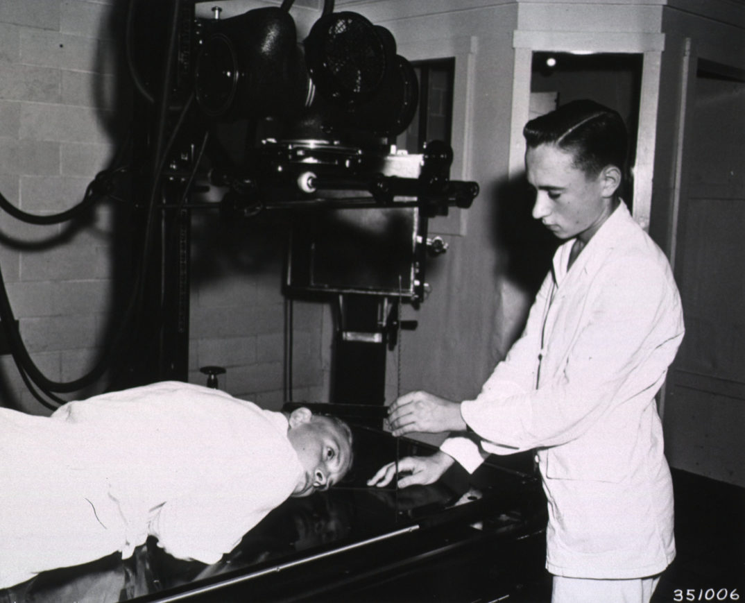 Black and white photograph of a medical student examining a person on a table