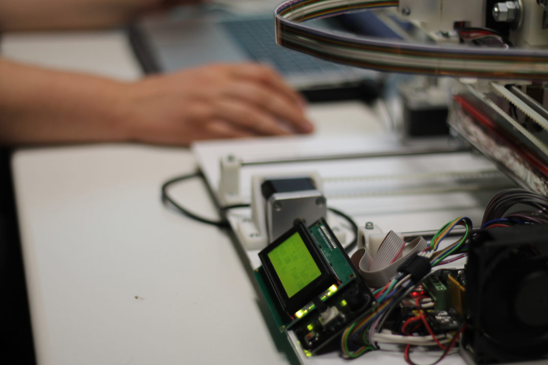 Photograph of a 3D printer with a person's hand on a computer mouse nearby