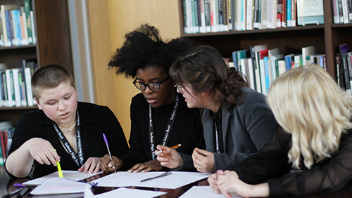 Four high school students sitting behind a table discussing their strategy at a high school ethics bowl competition at the Prindle Institute