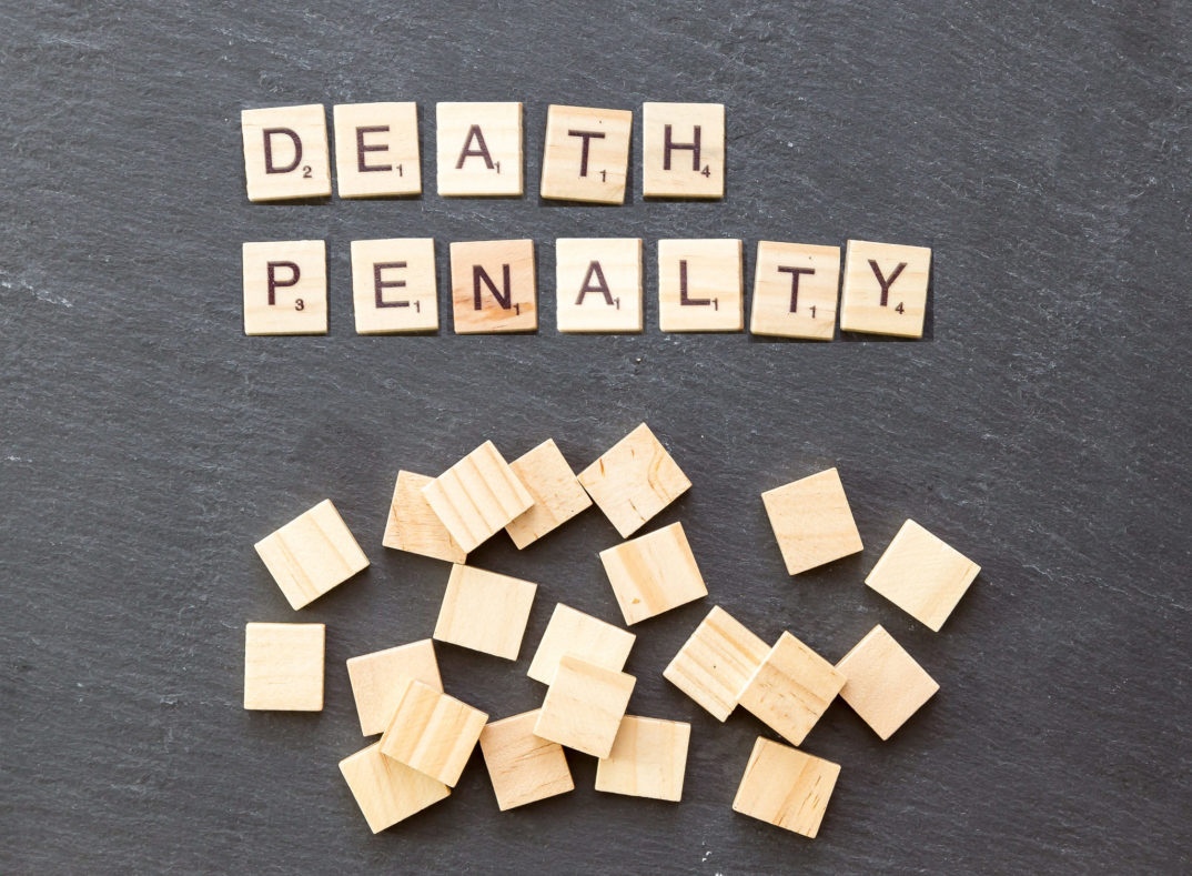 Scrabble tiles spelling out the phrase "Death Penalty" on a gray background