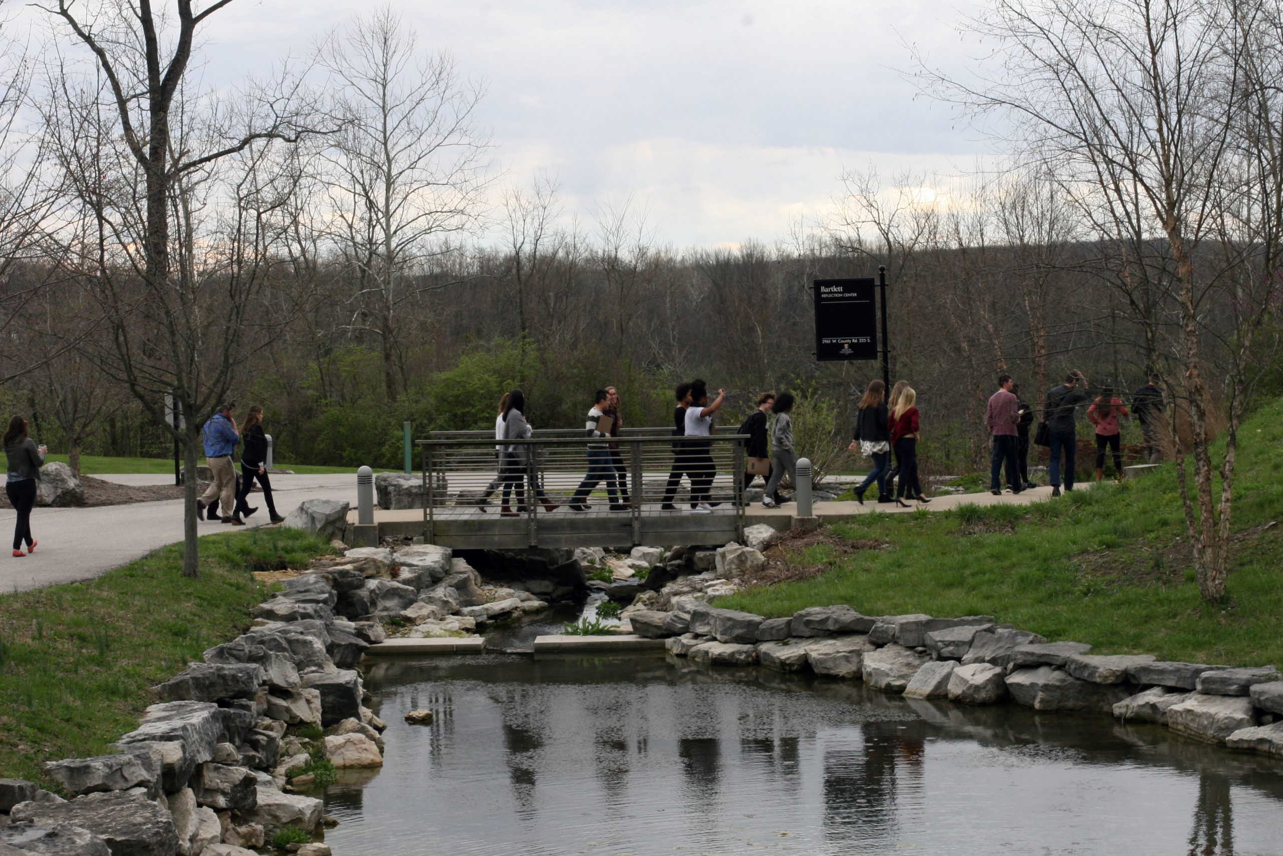 Large group of diverse undergraduate students walking across a small bridge over the Prindle Institute for Ethics' reflection pond.