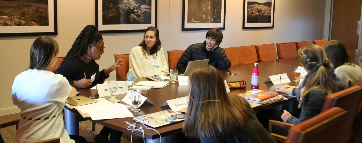 A professor and some of her students seated around a table in a heated discussion