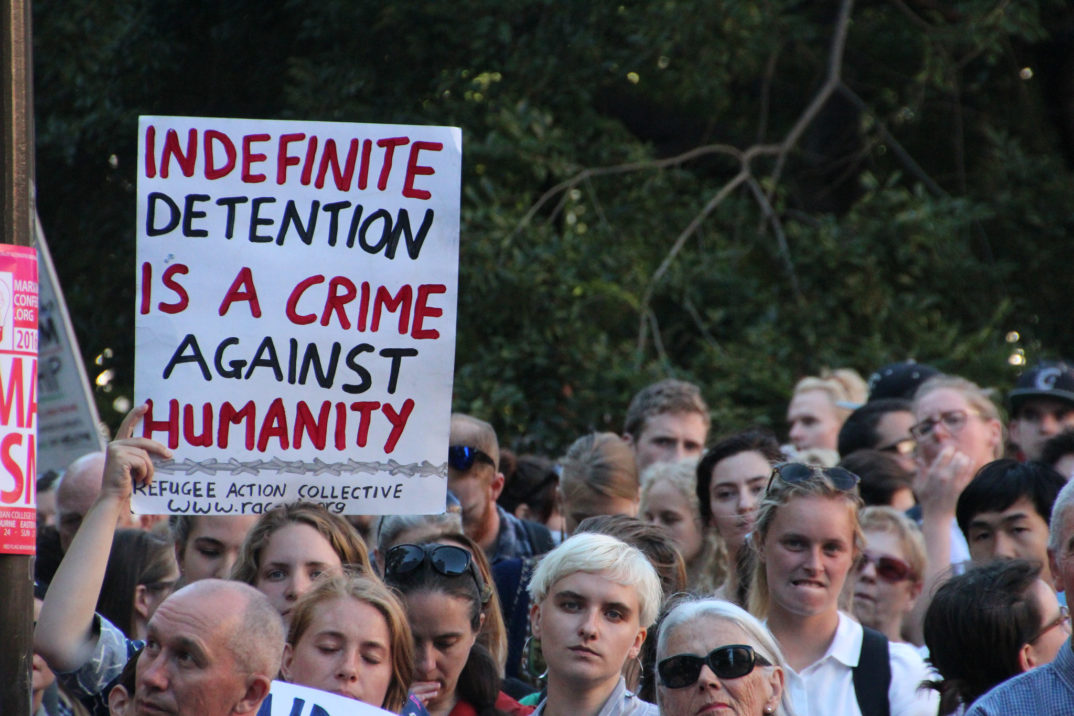 Photograph of a rally with a person holding a sign saying "Indefinite Detention is a crime against humanity"