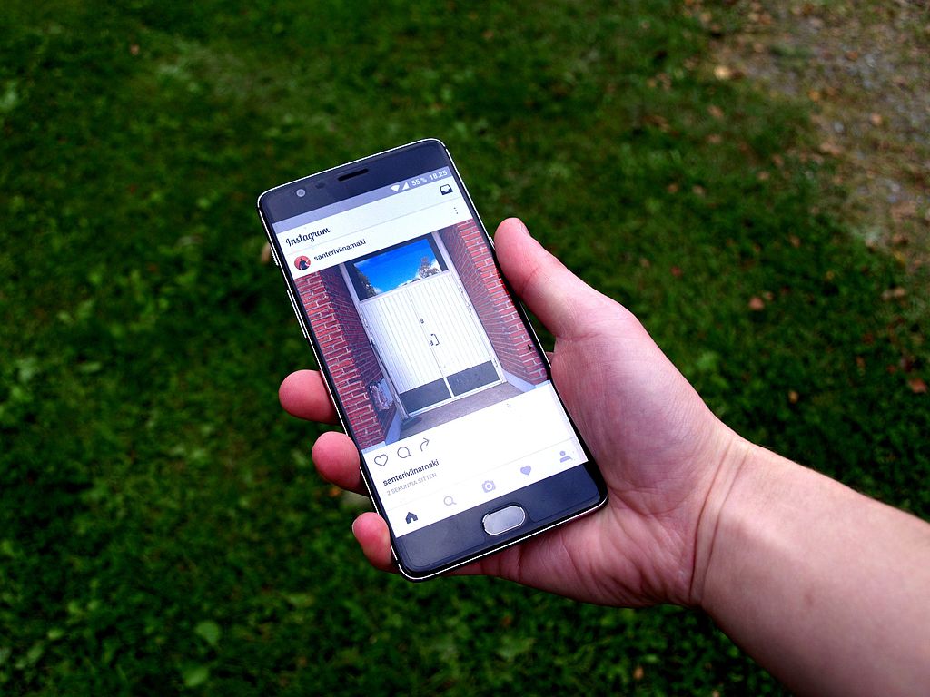 Photograph of a person holding a smartphone with Instagram showing on the screen
