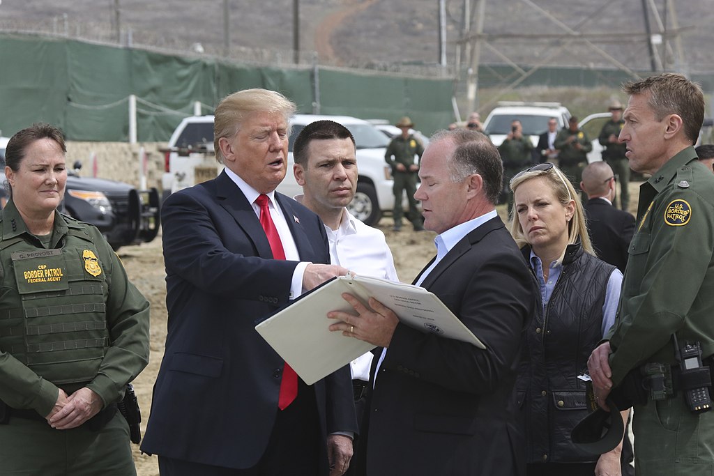 Photograph of President Trump looking at a book with other people gathered