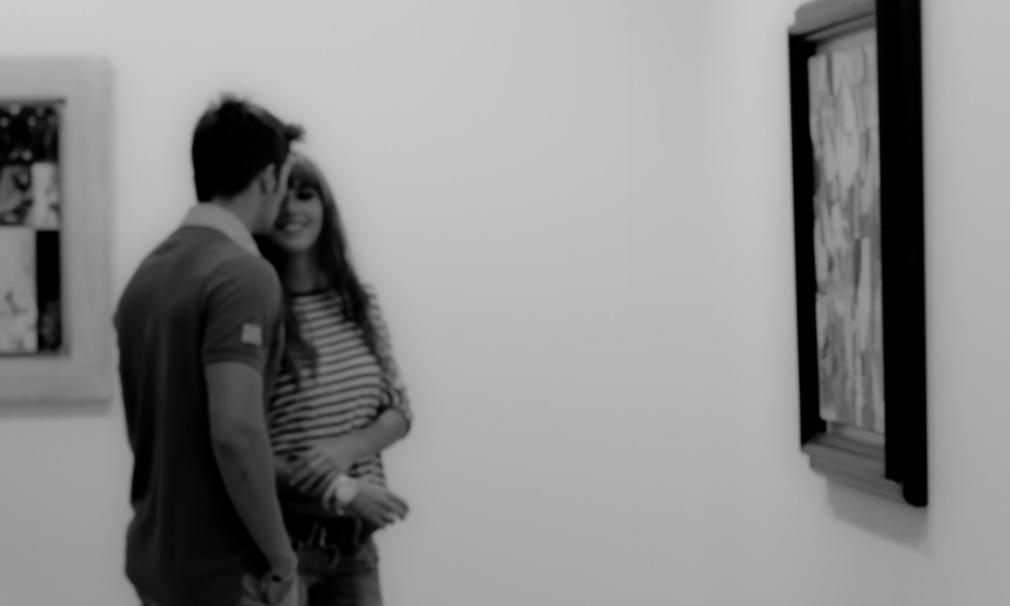 Black and white photograph of a couple in an art gallery, standing in front of a picture, the woman is laughing