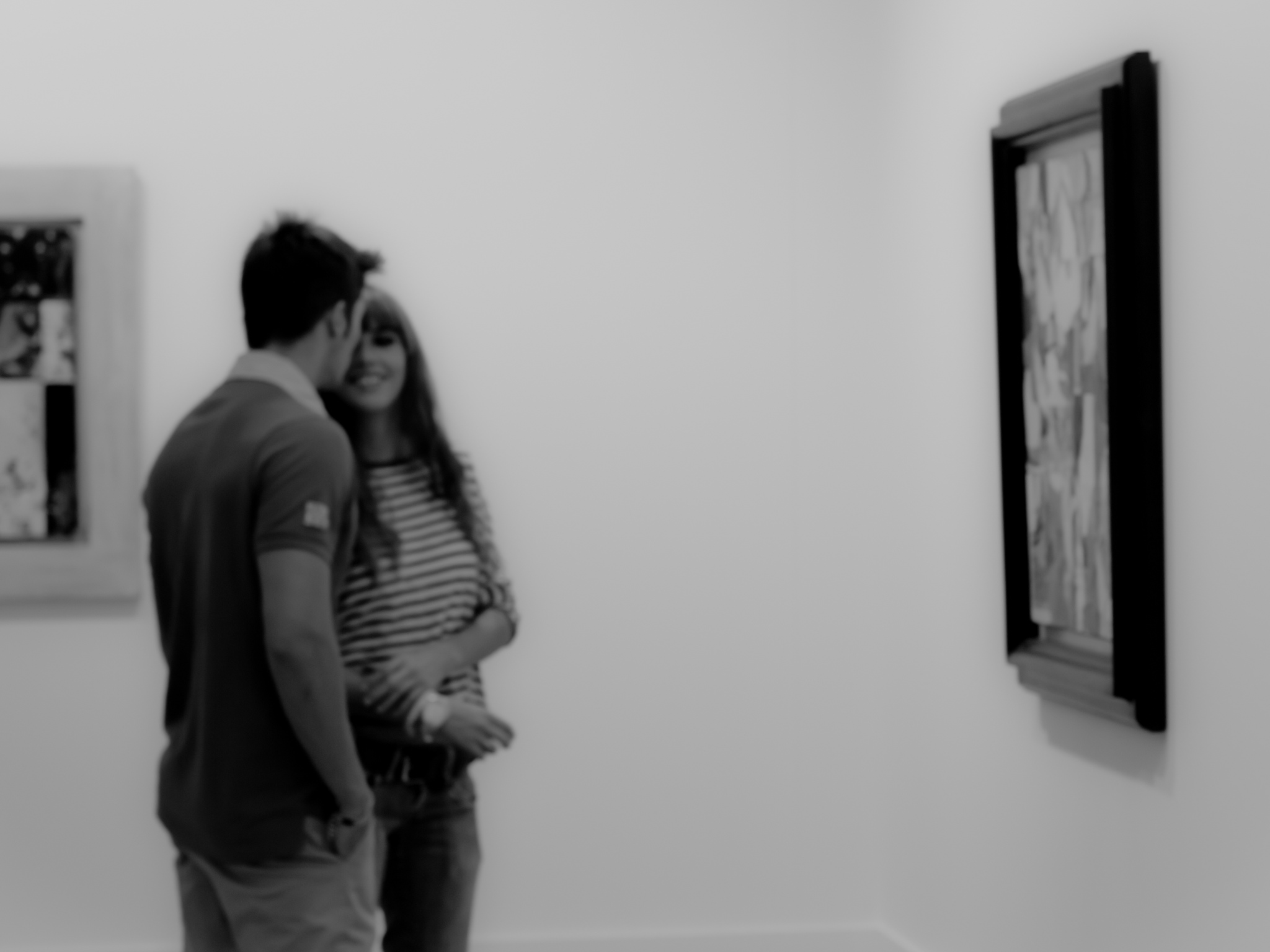 Black and white photograph of a couple in an art gallery, standing in front of a picture, the woman is laughing