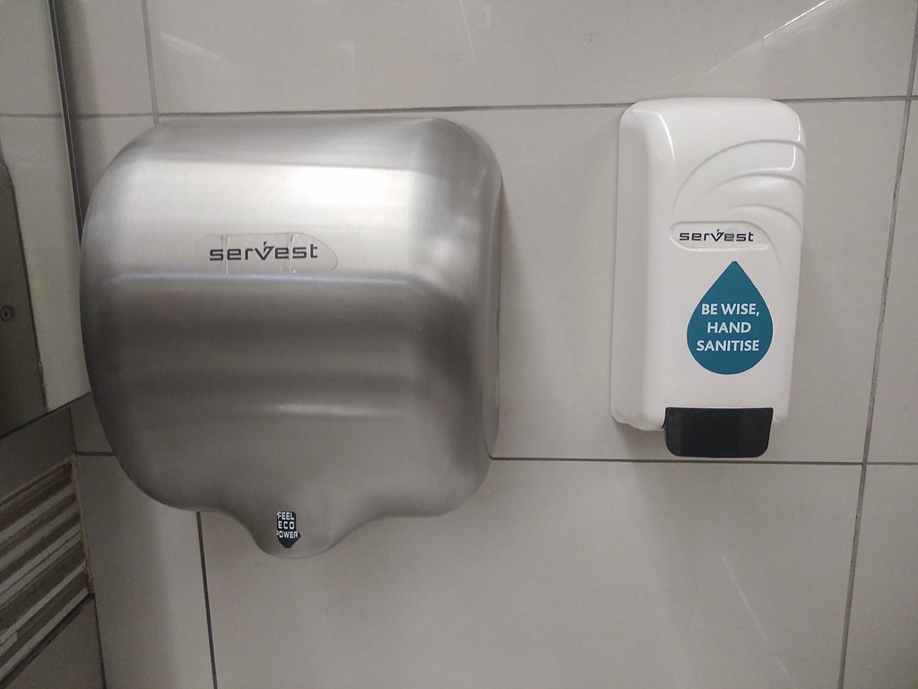 Photograph of a hand drier and a hand sanitizer dispenser attached to a tiled wall