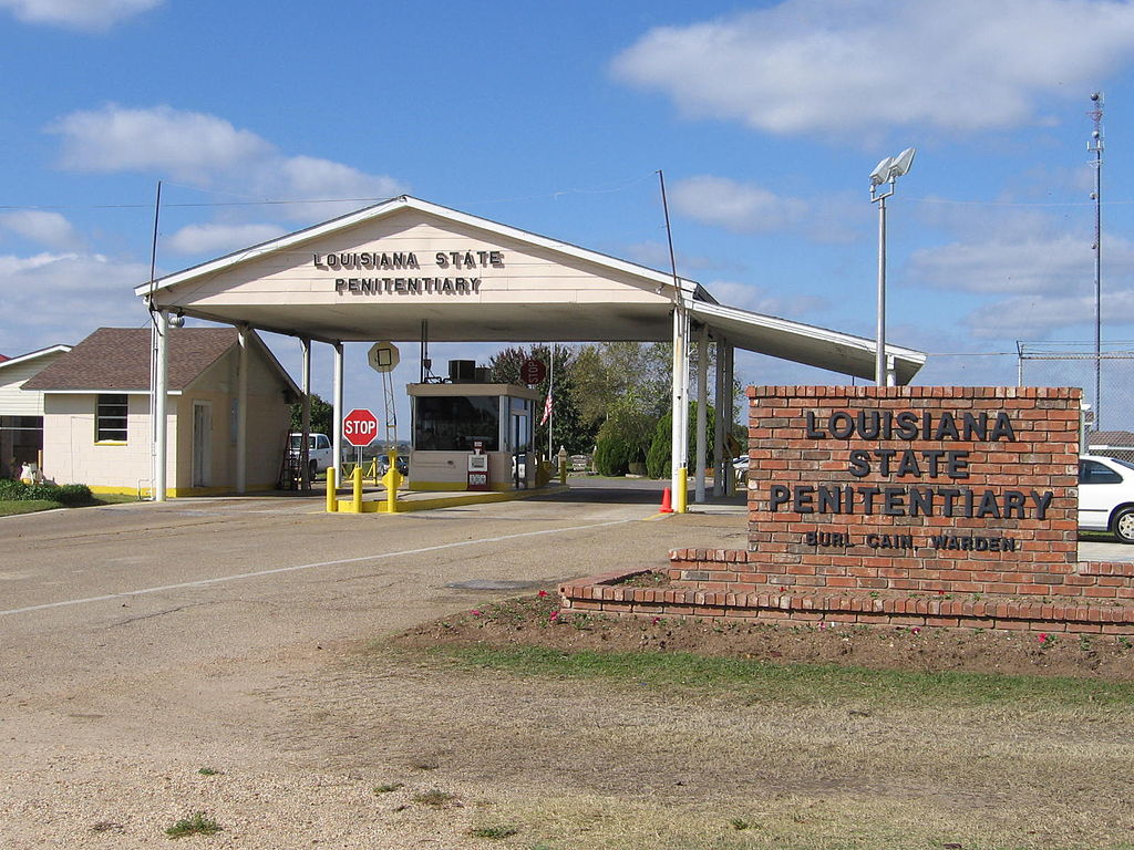 Photograph of the entrance to the Louisiana State Penitentiary, showing a stop sign and a guard station along with a sign naming the institution and the warden Burl Cain