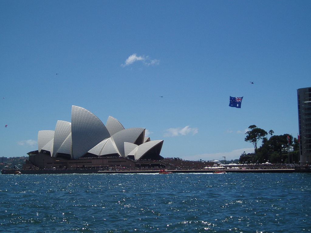 Photo of the Sydney Harbor overlooking the Opera House and an Australian flag flying in the sky from a plane