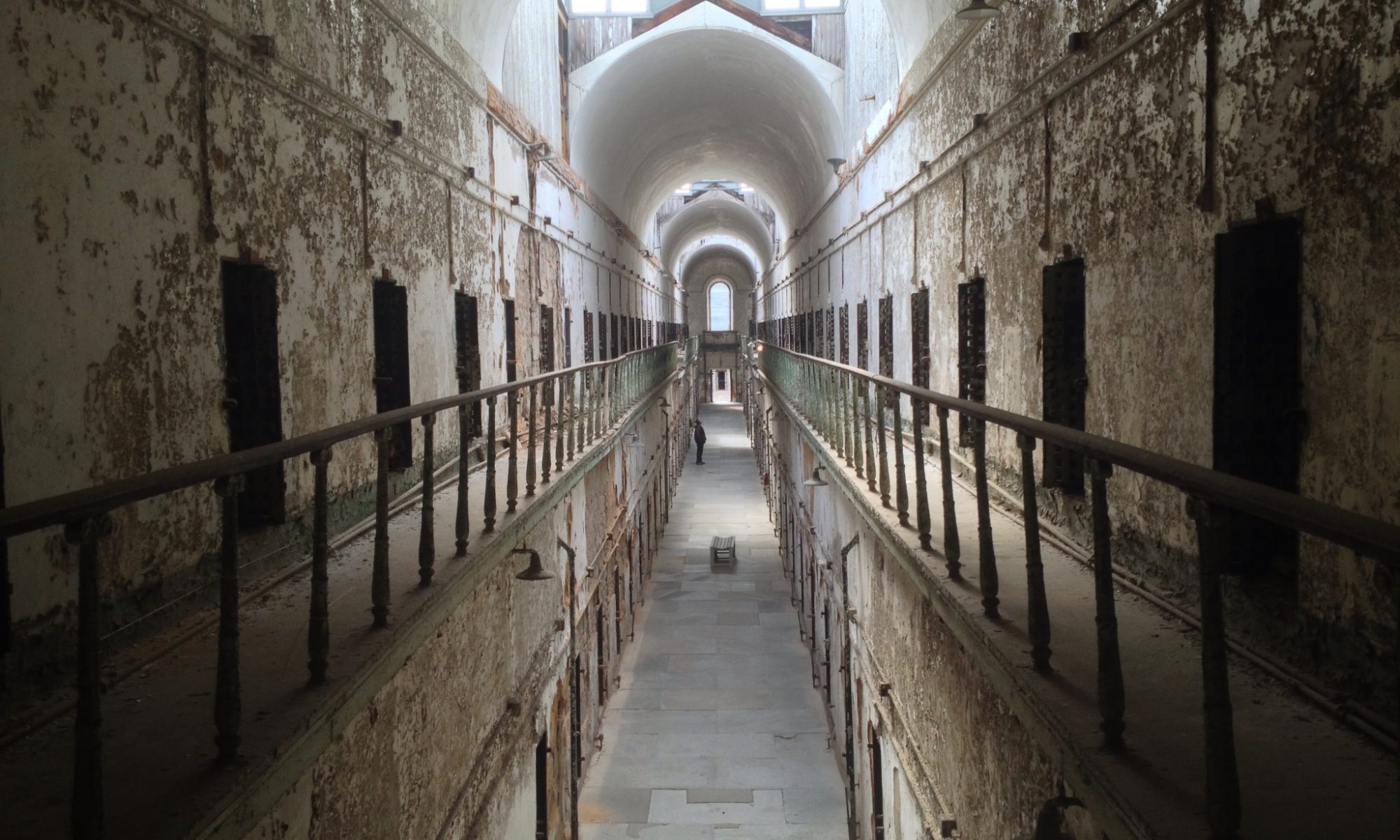 Photograph of a long hall of cells with light and a dome at the end