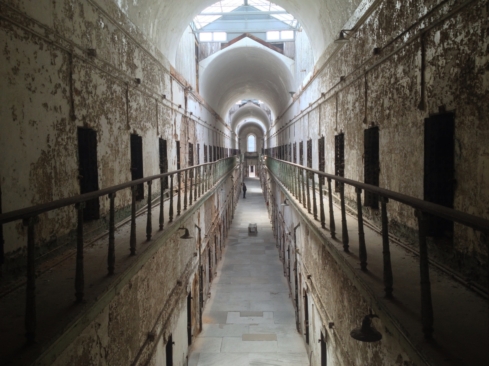 Photograph of a long hall of cells with light and a dome at the end