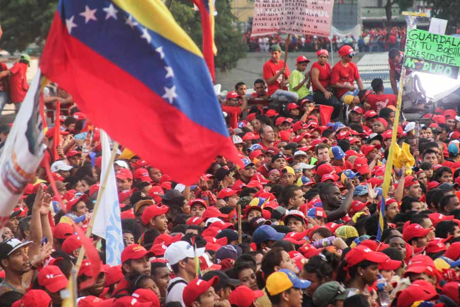 Photograph of a Venezuelan flag in the foreground and a crowd of protesting people in the background
