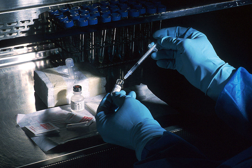Photograph of hands of a scientist, under a sterile hood, preparing a vaccine