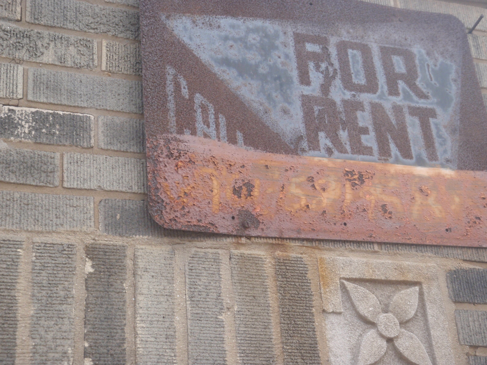 A rusted red sign that says For Rent