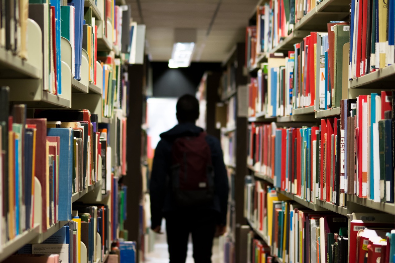 A boy walks through an aisle of books in a library.