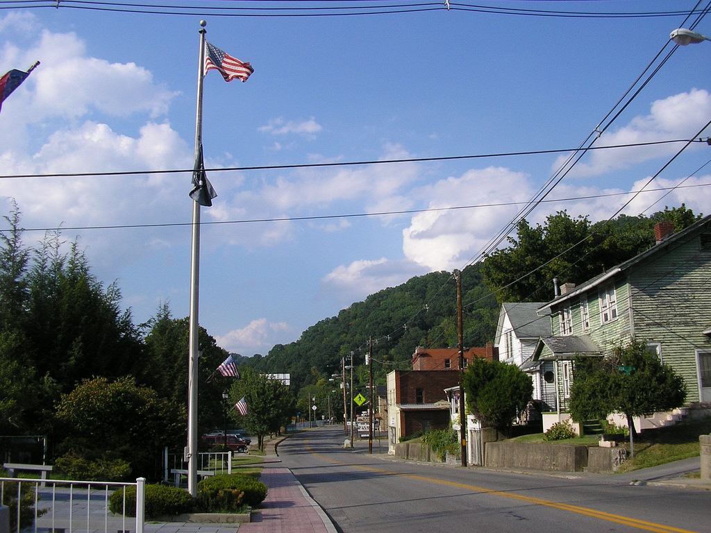 A small town main street with a green mountain in the background and an American flag
