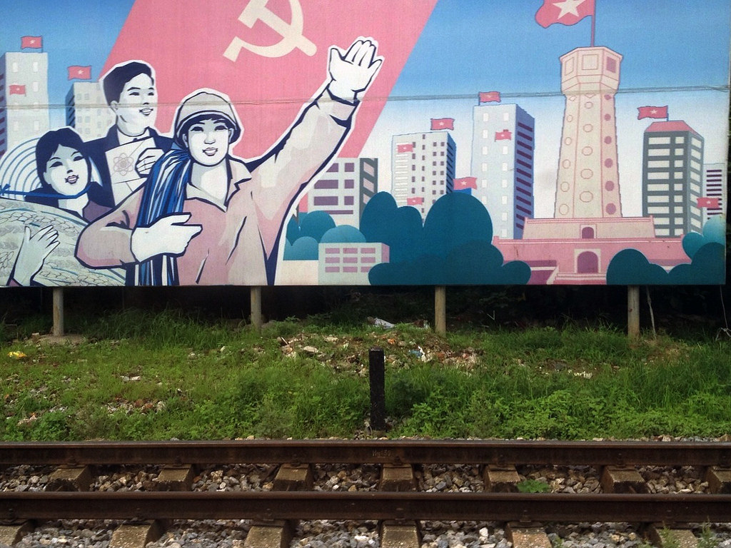 Graffiti image of three happy individuals under communist flag with Vietnam skyline behind