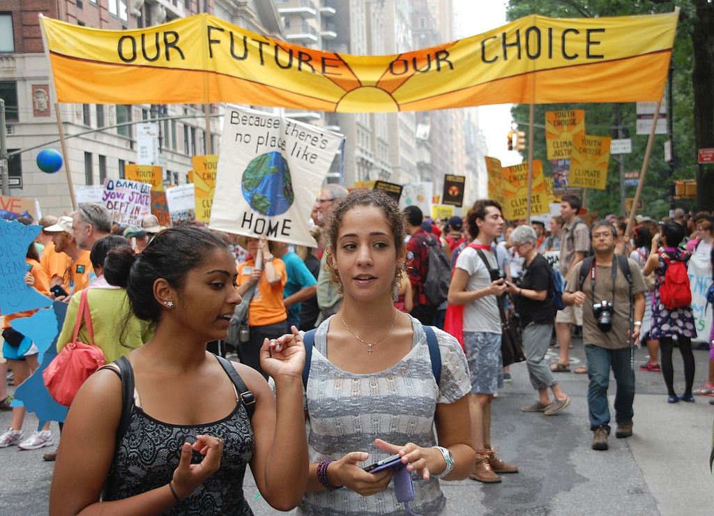 Two young women in the foreground of a protest march, with signs behind them saying "our future our choice"