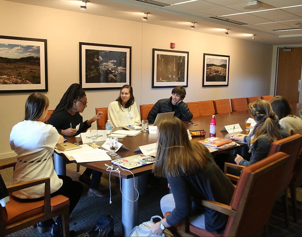 Students and their professor sit around a wooden table in discussion.