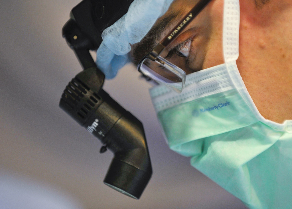 close-up photograph of physician's face with mask and headlamp