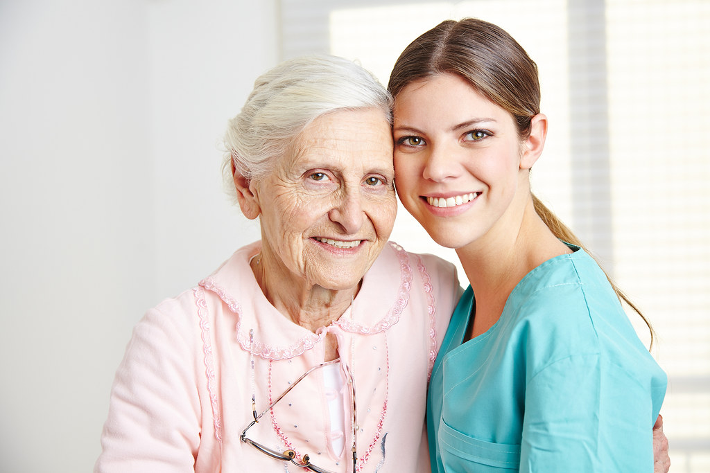 Smiling caregiver embracing happy senior woman in nursing home