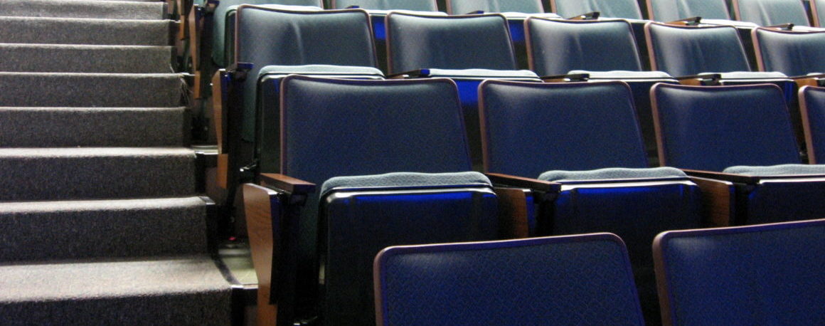 Many rows of empty blue vinyl seats in a classroom auditorium