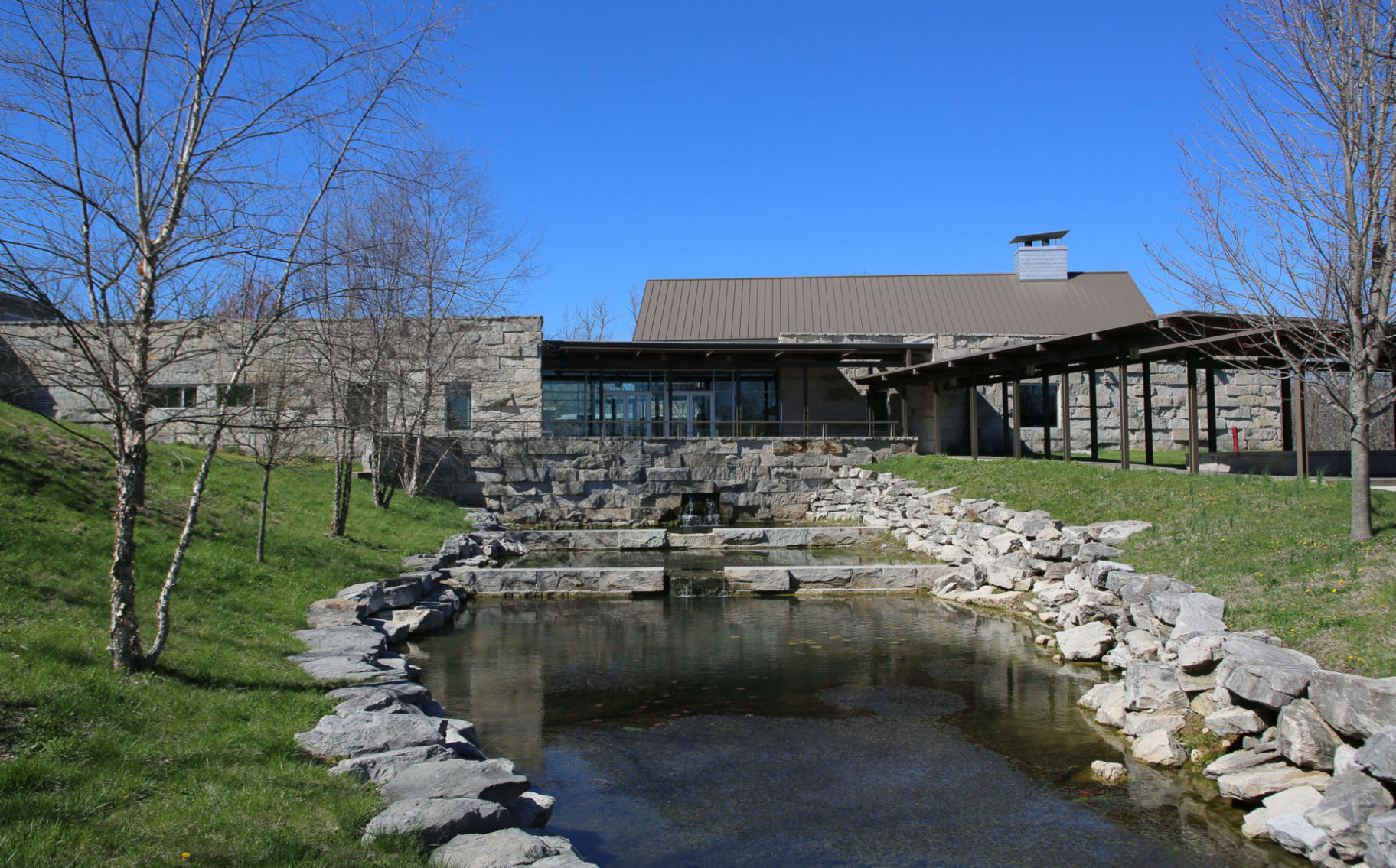 A large stone and wooden structure with a tiered waterfall feature in the ground in front of it.
