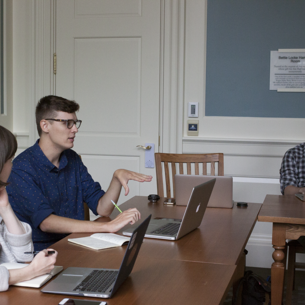Man sits behind a computer and gesticulates in a conference room