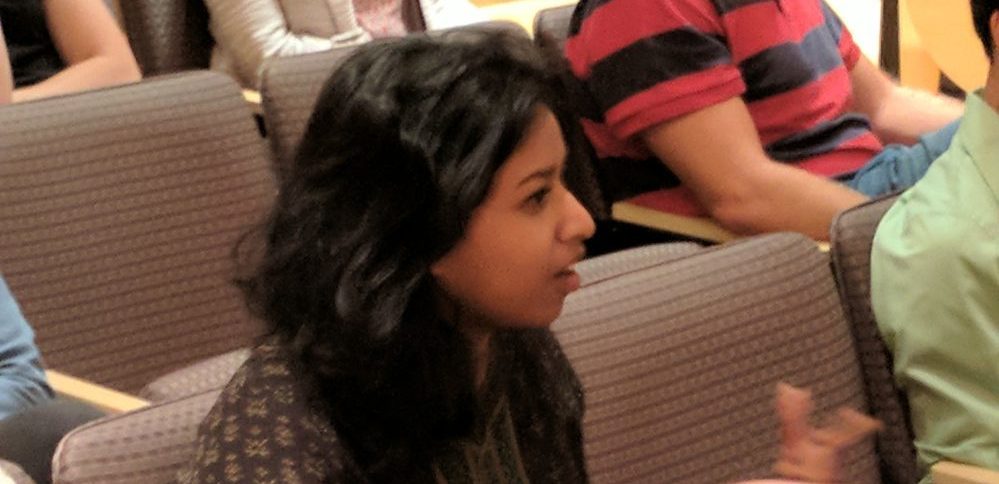 A woman in a crowded auditorium asks a question of the speaker who is off camera