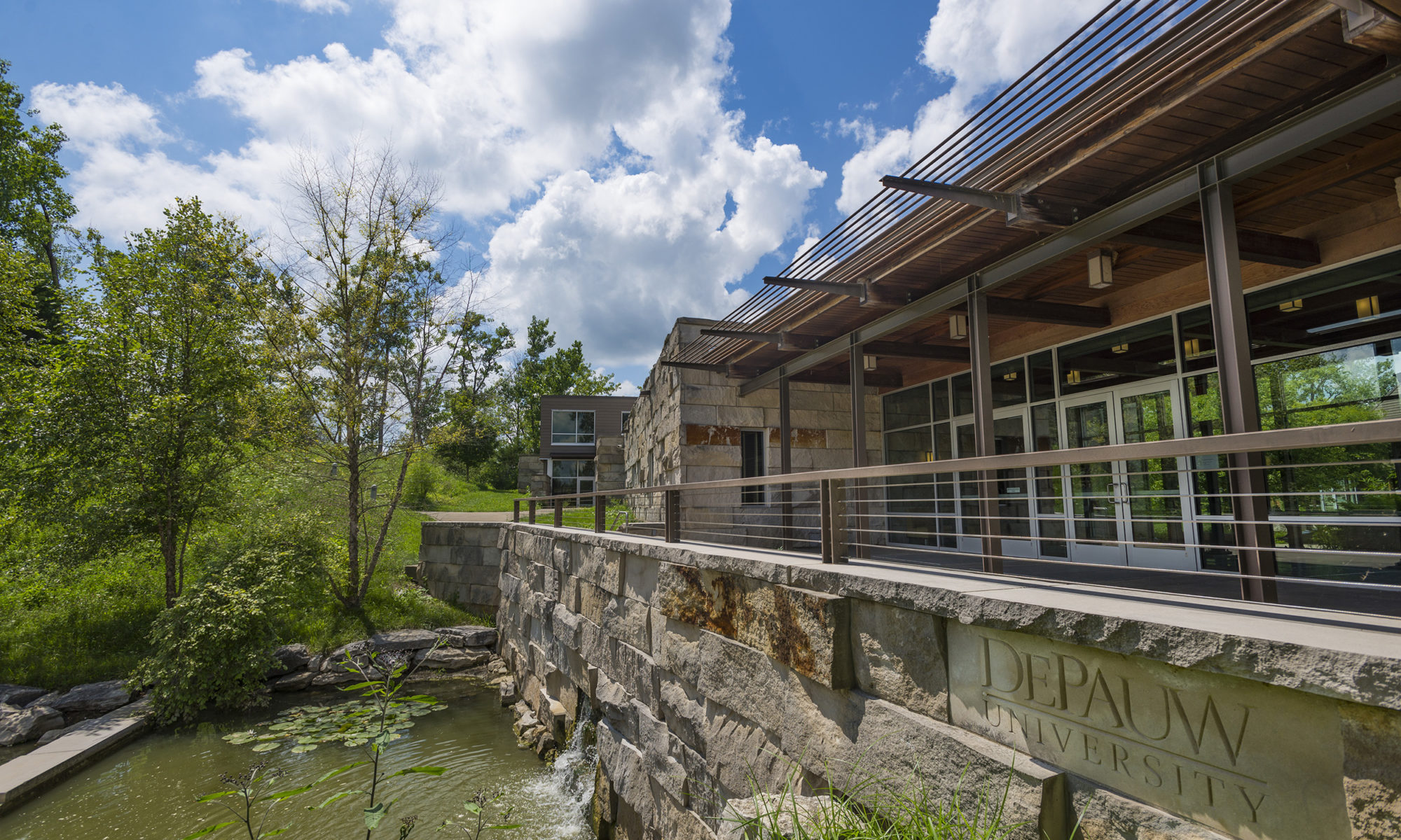 Large stone, wooden and glass structure. You can see the entrance, but also the water feature in the front of the building