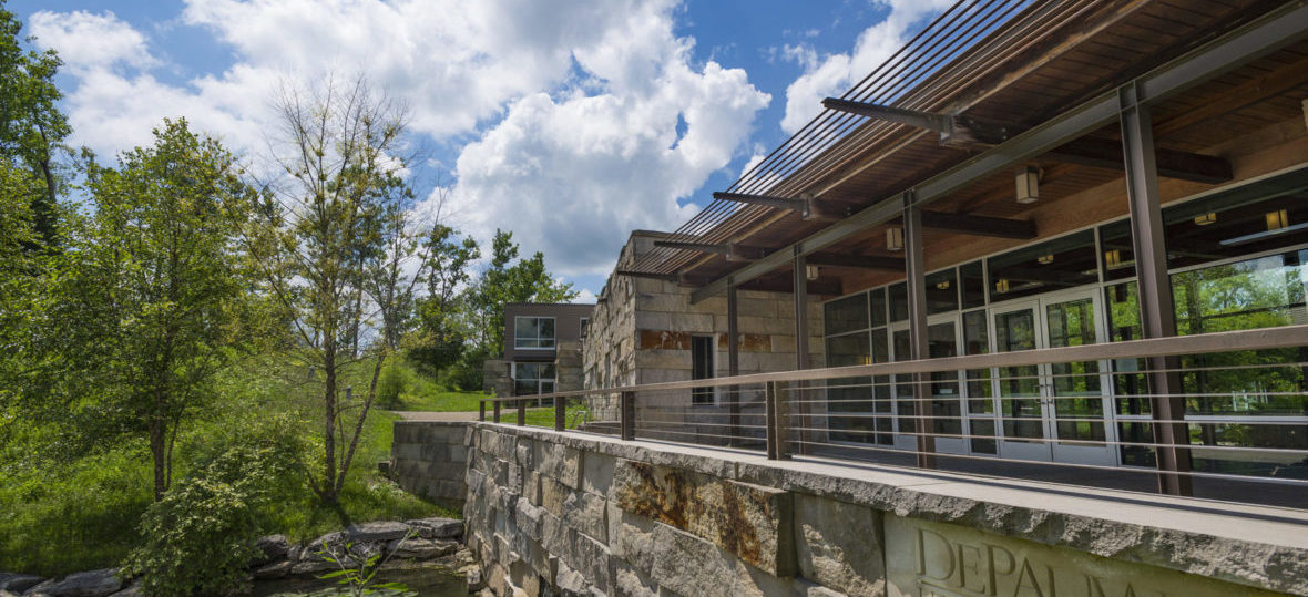 Large stone, wooden and glass structure. You can see the entrance, but also the water feature in the front of the building