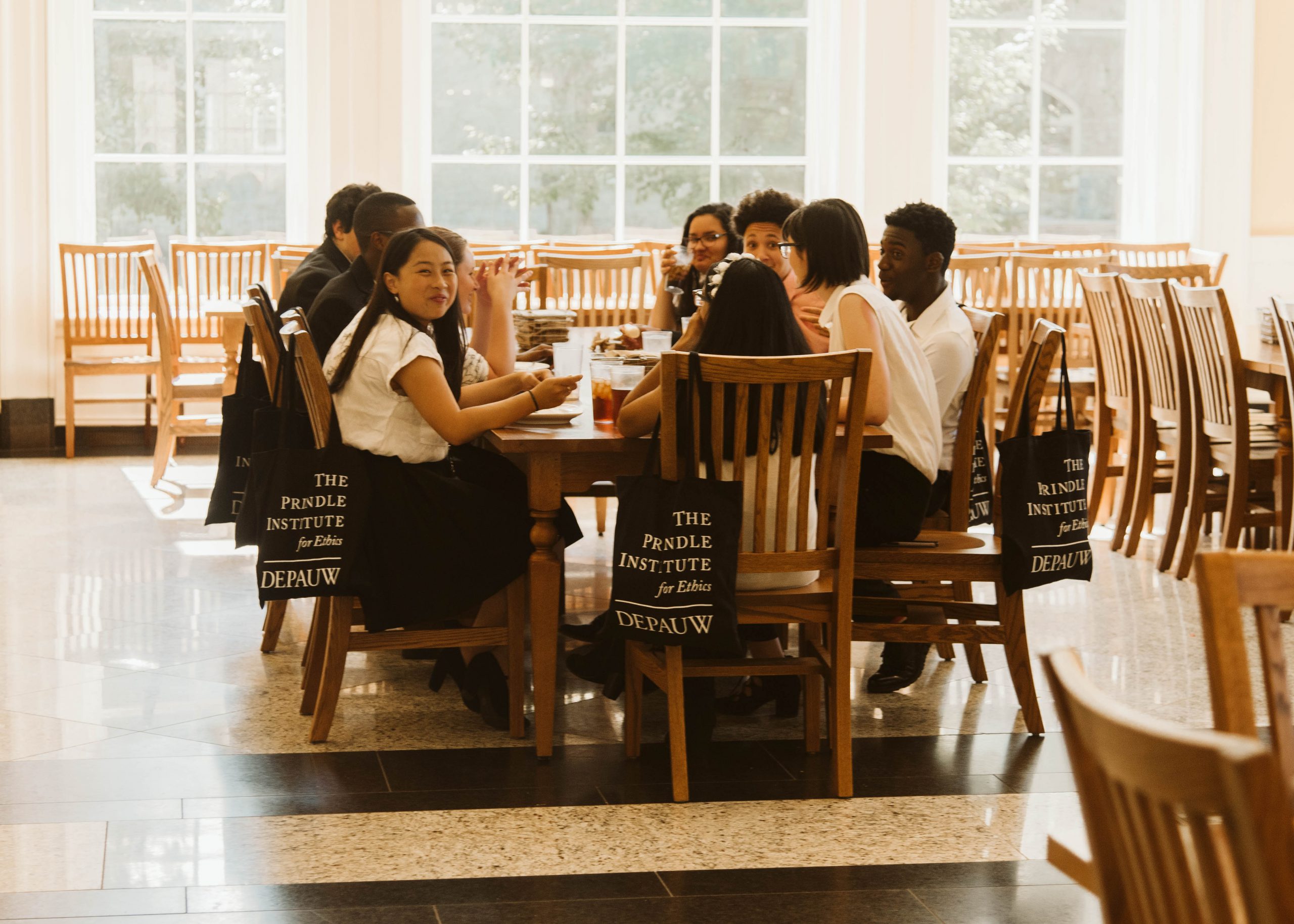A group of high school students seated around a table in a large dining hall. One student is looking at the camera and smiling.