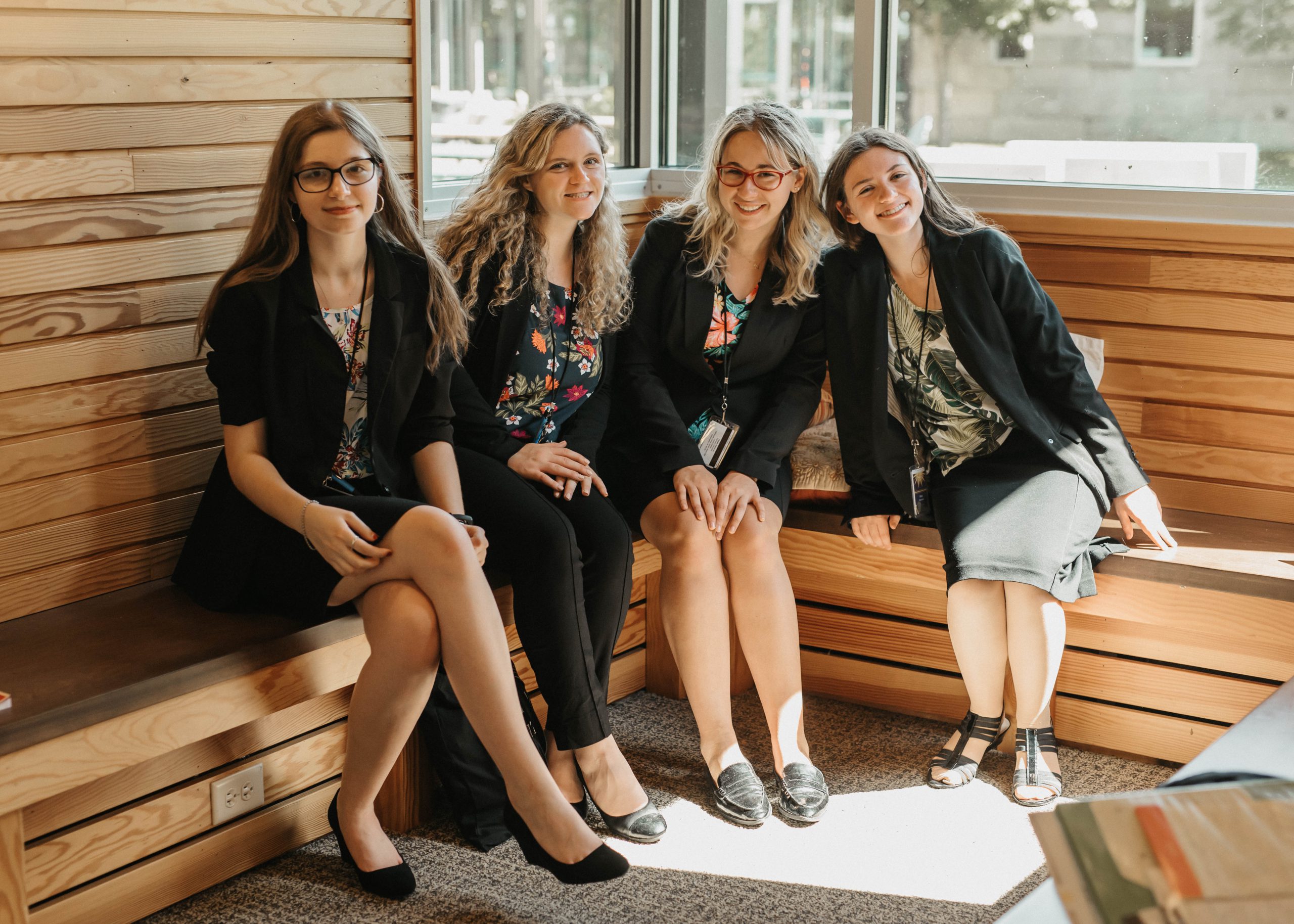 A group of high school-aged women seated in a nook at the Prindle Institute. They are all smiling for the camera.