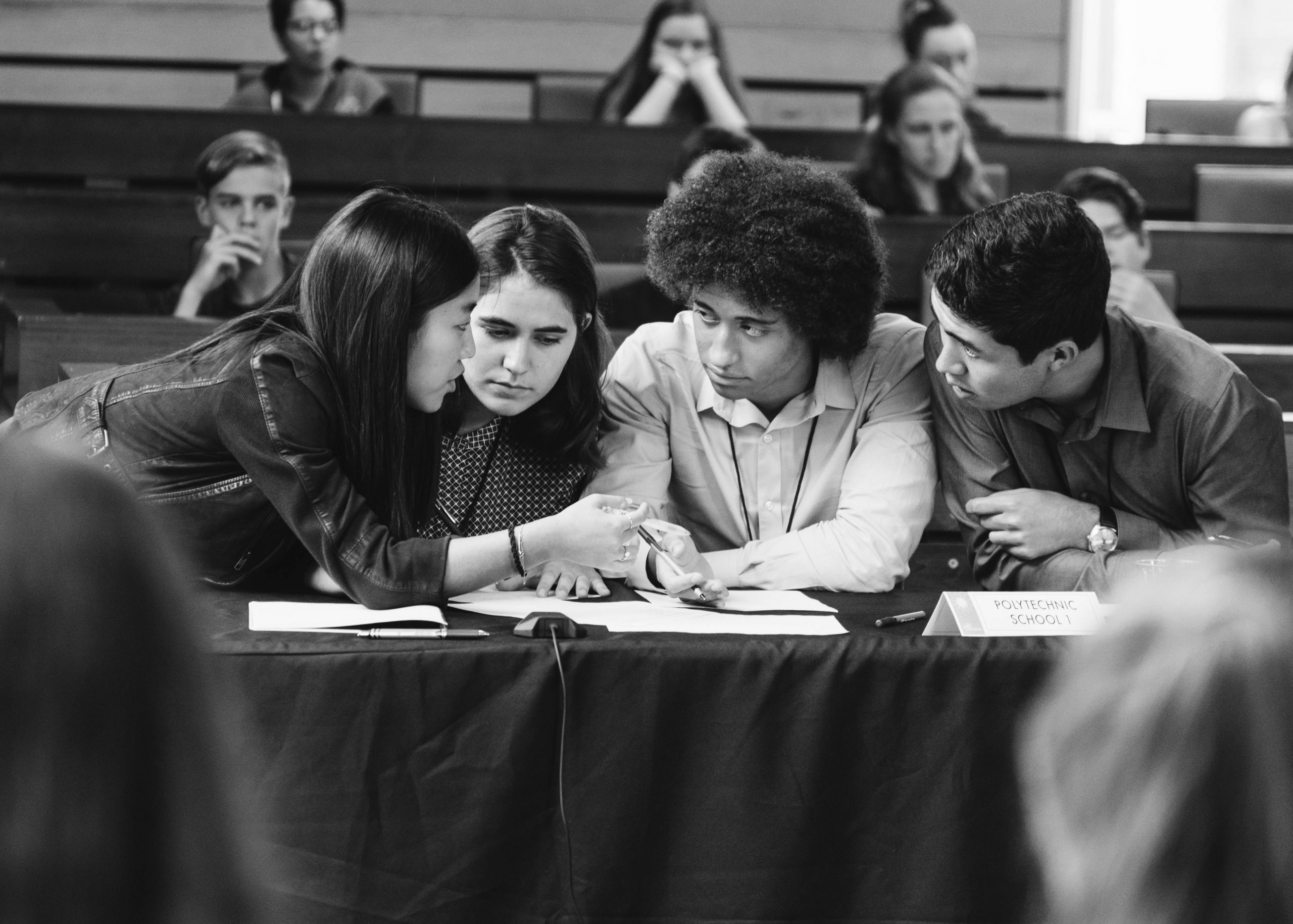 Four high school students sit behind a table, and engage in a serious discussion