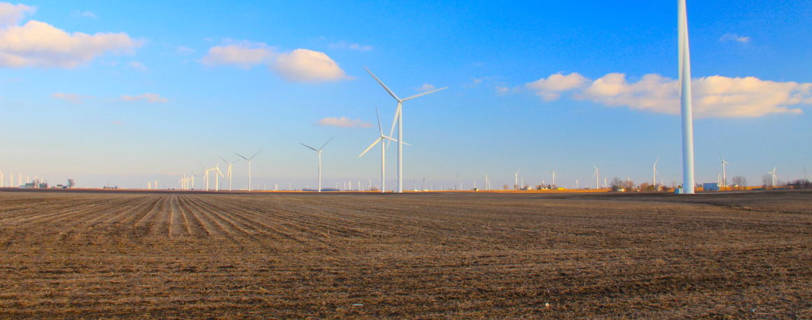 Blue skies above a large brown agricultural field filled with large wind turbines.