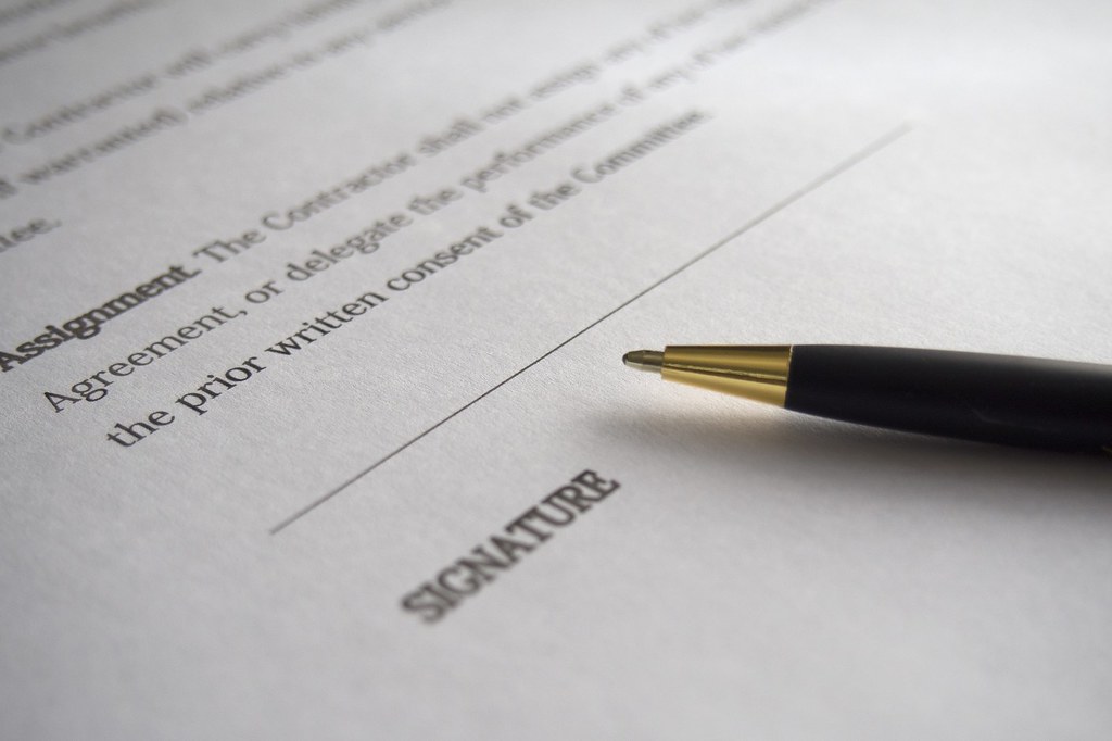 close-up photograph of contract with pen laying on "signature" section